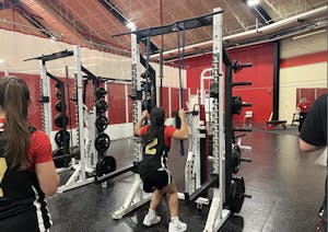 A woman wearing a basketball jersey with the number 2 uses a weight machine at a gym.