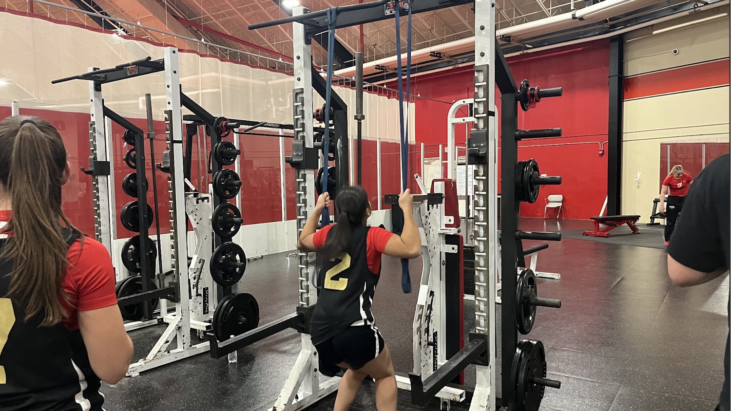A woman wearing a basketball jersey with the number 2 uses a weight machine at a gym.