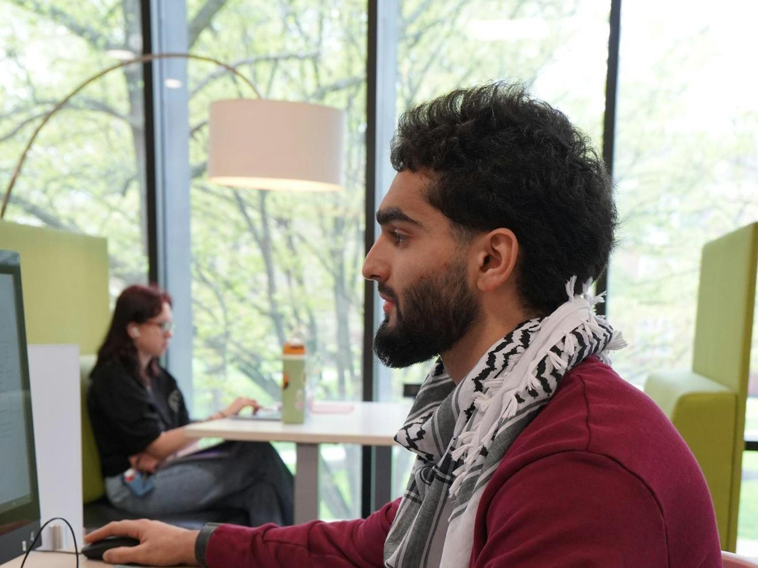 Student working on homework in the library. He is shown wearing a keffiyeh. 