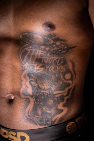 Rib cage tattoo that says "The World Is Yours," with stars and planets surrounding it.