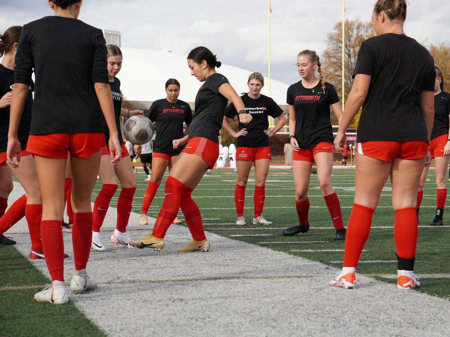 Nine female soccer players juggle the soccer ball amongst one another. 