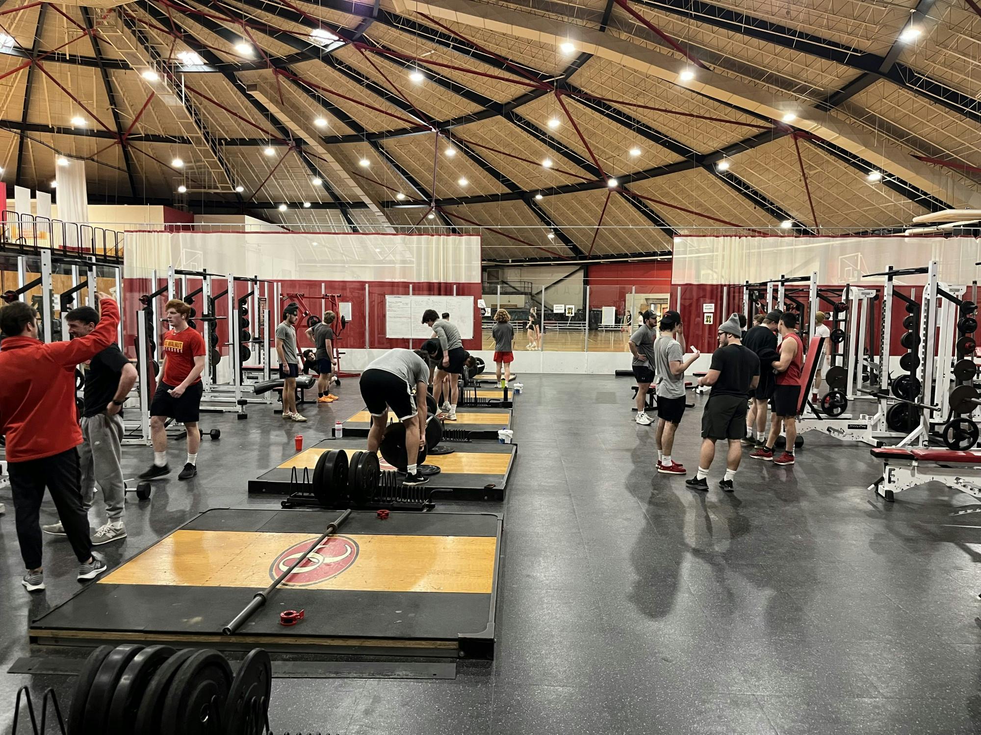 A group of people stand in the Rike Center weight room, either talking or actively using equipment.