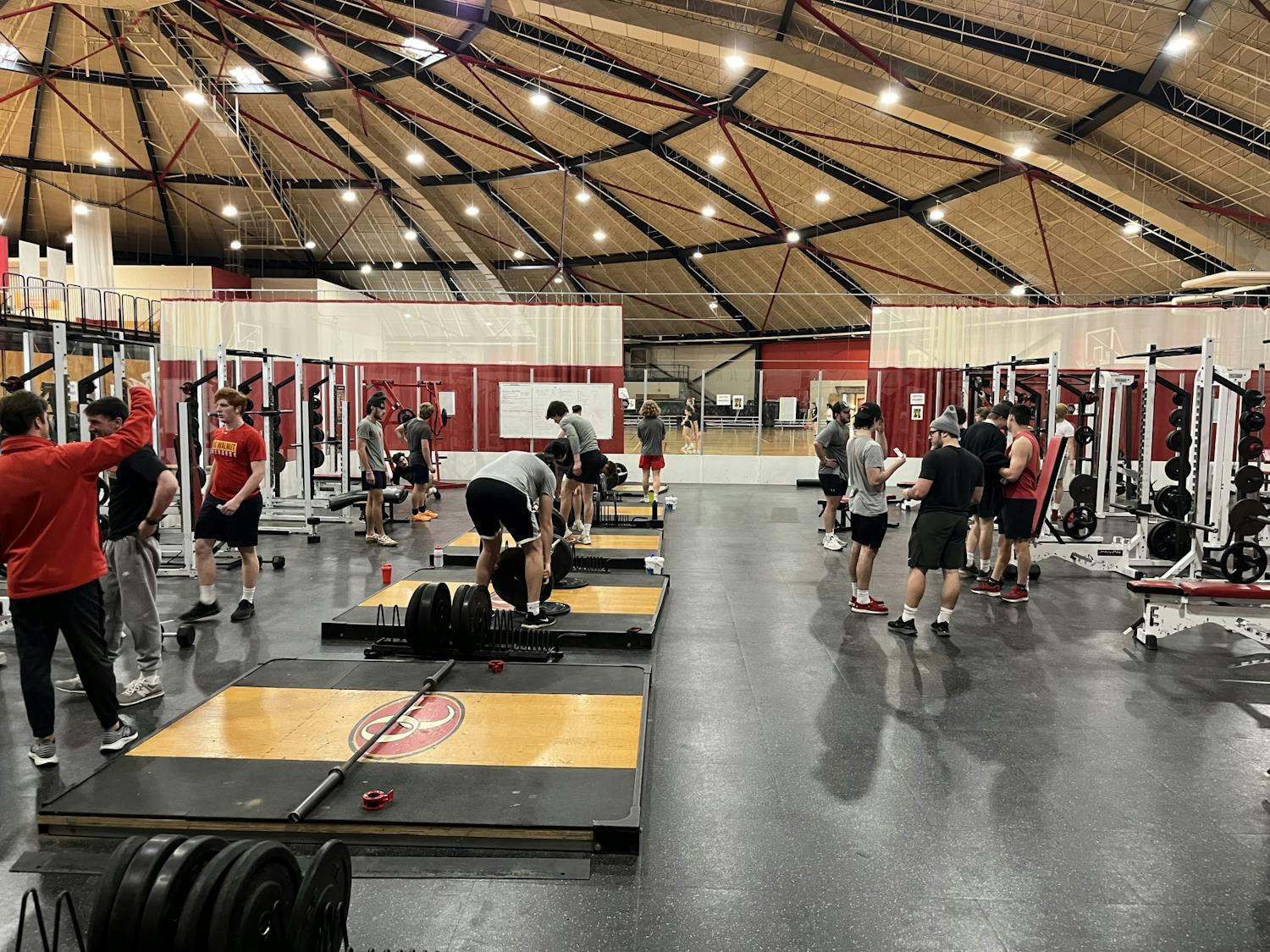 A group of people stand in the Rike Center weight room, either talking or actively using equipment.
