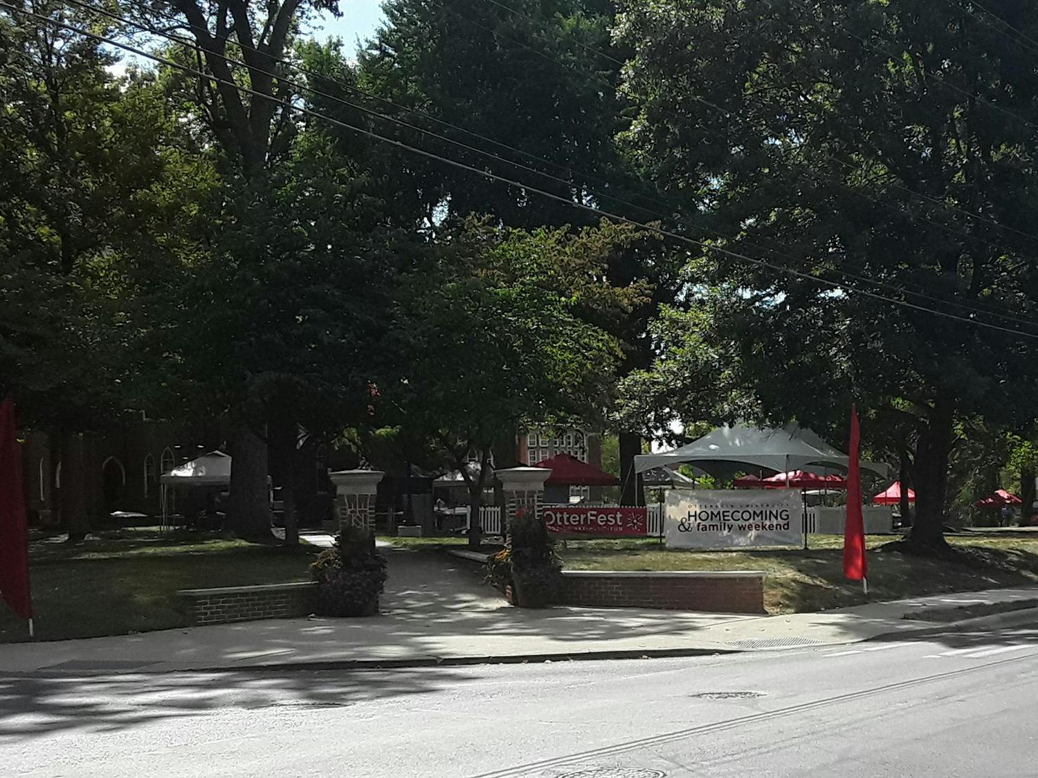 Red and white outdoor tents set up on grass in front of brick building. A red banner reads "OtterFest" and a white banner reads "Homecoming and Family Weekend."