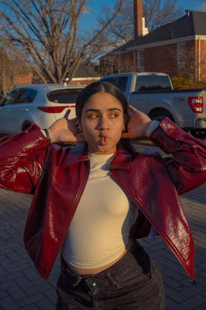 Dark haired girl wearing a maroon jacket and a light-colored shirt posing looking away doing a facial expression.