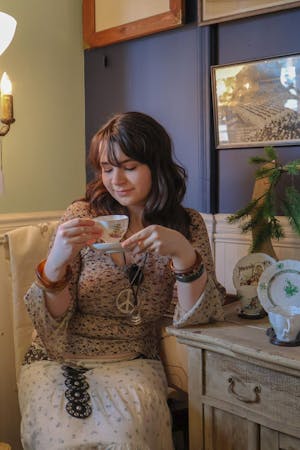 Brown haired girl wearing a white blouse lifting her teacup to drink.