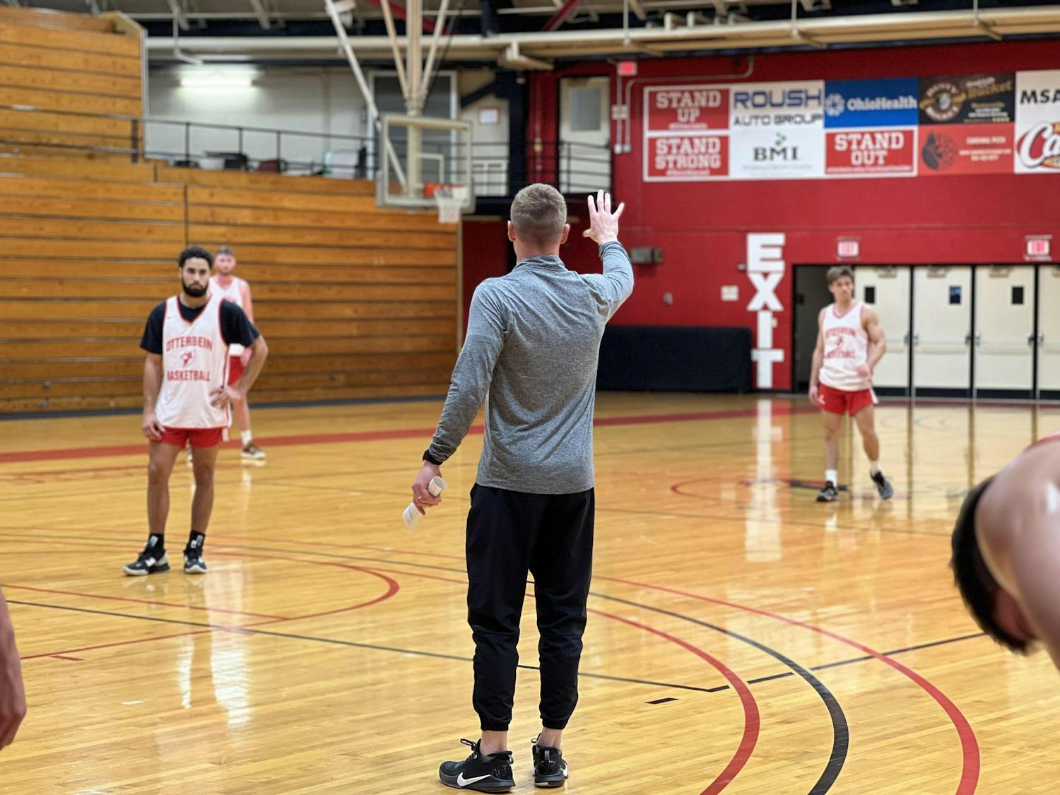 The head coach of the Otterbein men's basketball team directs three players in the distance.