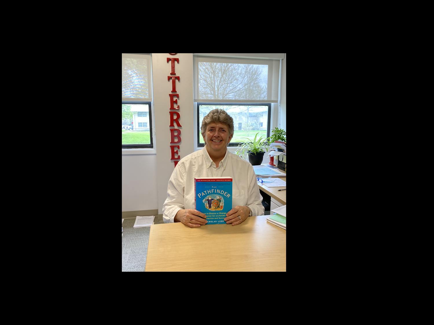 Female Otterbein University professor sitting at her desk In her office holding her copy of The Pathfinder: How to Choose or Change Your Career for a Lifetime of Satisfaction and Success by Nicholas Lore 