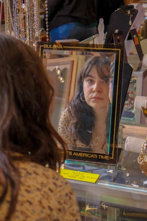 Brown haired girl wearing a blouse and earrings looking at her reflection in a mirror.