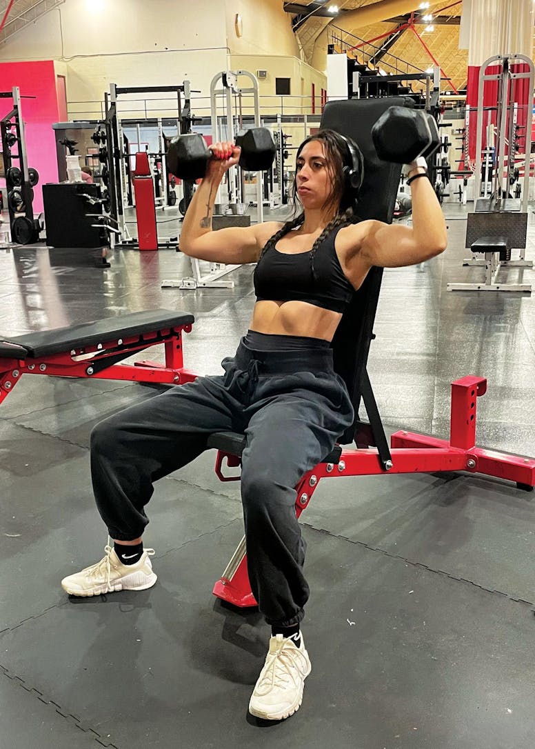 A seated women lifting dumbbells over her head.