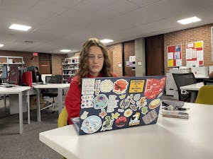 A girl with ginger hair and a red sweatshirt is sitting in front of a computer with many stickers on it. 