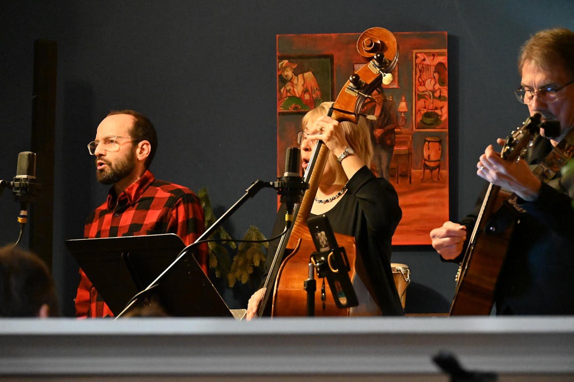 Three people are performing music, with singing and playing of the bass and guitar