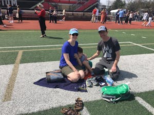 Photo of a man, woman, and child sitting on the turf of a football field.