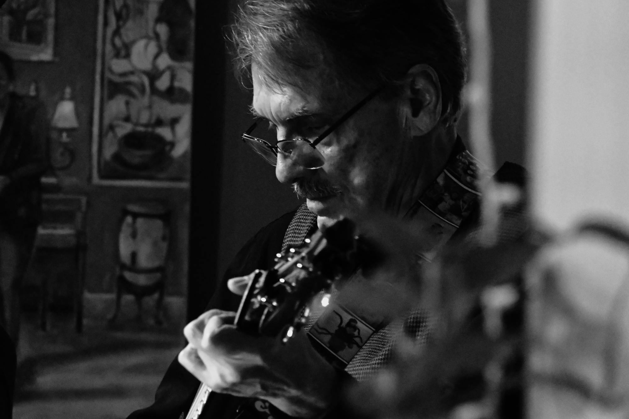 Black and white photo of a man playing guitar on the stage of Java Central. 
