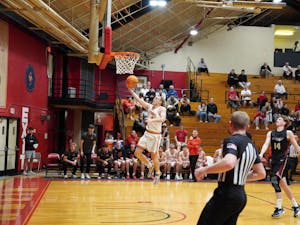 Jack Clement, an Otterbein basketball player goes for a layup as Jackson Rhodes, an Earlham College player looks on. A referee's back is towards the camera.
