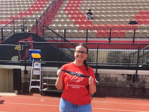 Girl in a red shirt that reads 'OTTERBEIN ECLIPSE TEAM 04.08.2024' in white lettering. She is smiling and holding up a pair of solar eclipse sunglasses.