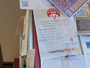 A flyer promoting the Otterbein SAFE app is pinned to a bulletin board with many other flyers around it.