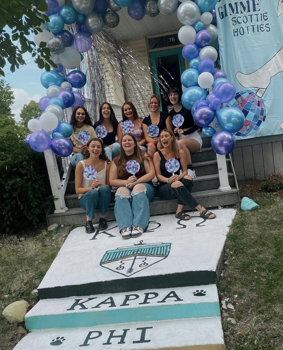 Eight new members of the Kappa Phi Omega sorority smile and sit on the steps of the house.