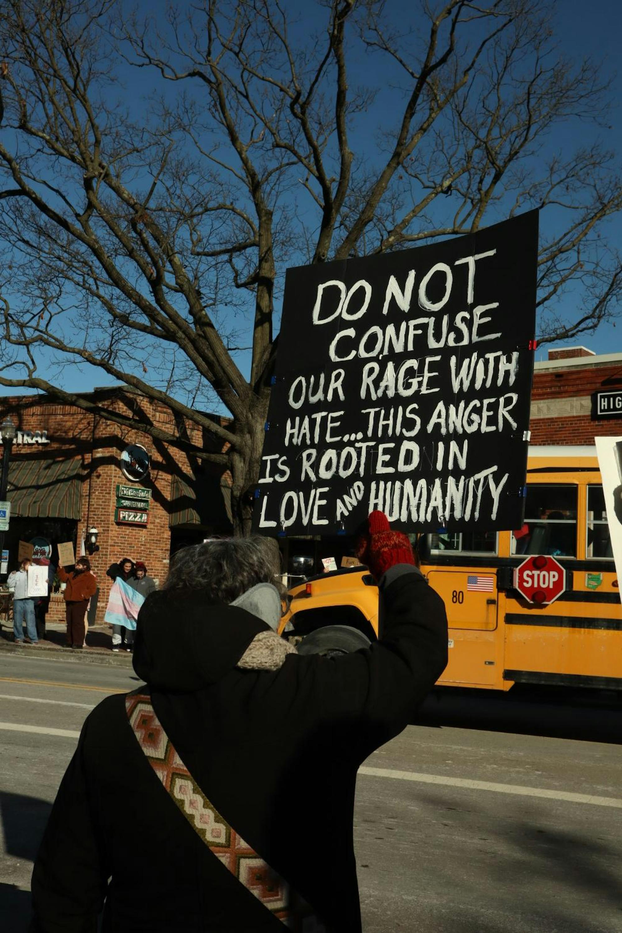 A person holding a sign in the air in front of a school bus.