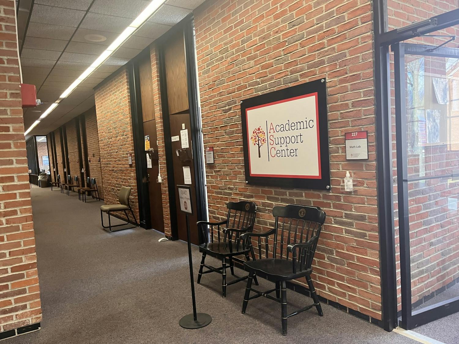 Brick walls surround a hallway with black chairs in them, and a sign that reads "Academic Support Center."