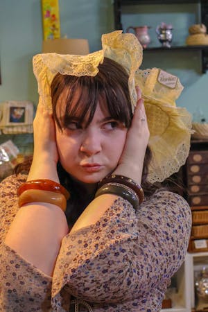 Head shot of a girl with bracelets looking away from the camera posing with hands on her head.