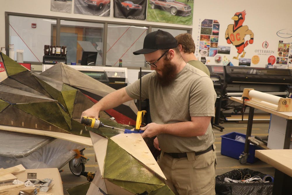 Max Sprowl using a power drill to secure a wooden panel on the dragon's head