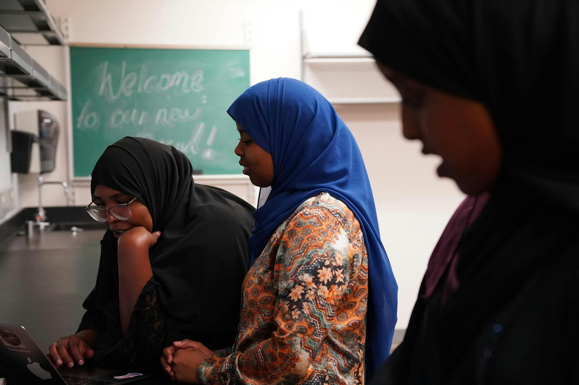 Three female students talk with one another and look at content on a computer in the new mosque. 