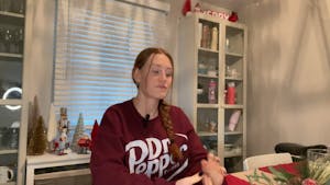 A girl with ginger hair and a maroon sweatshirt sits at a wooden table and answers questions. 