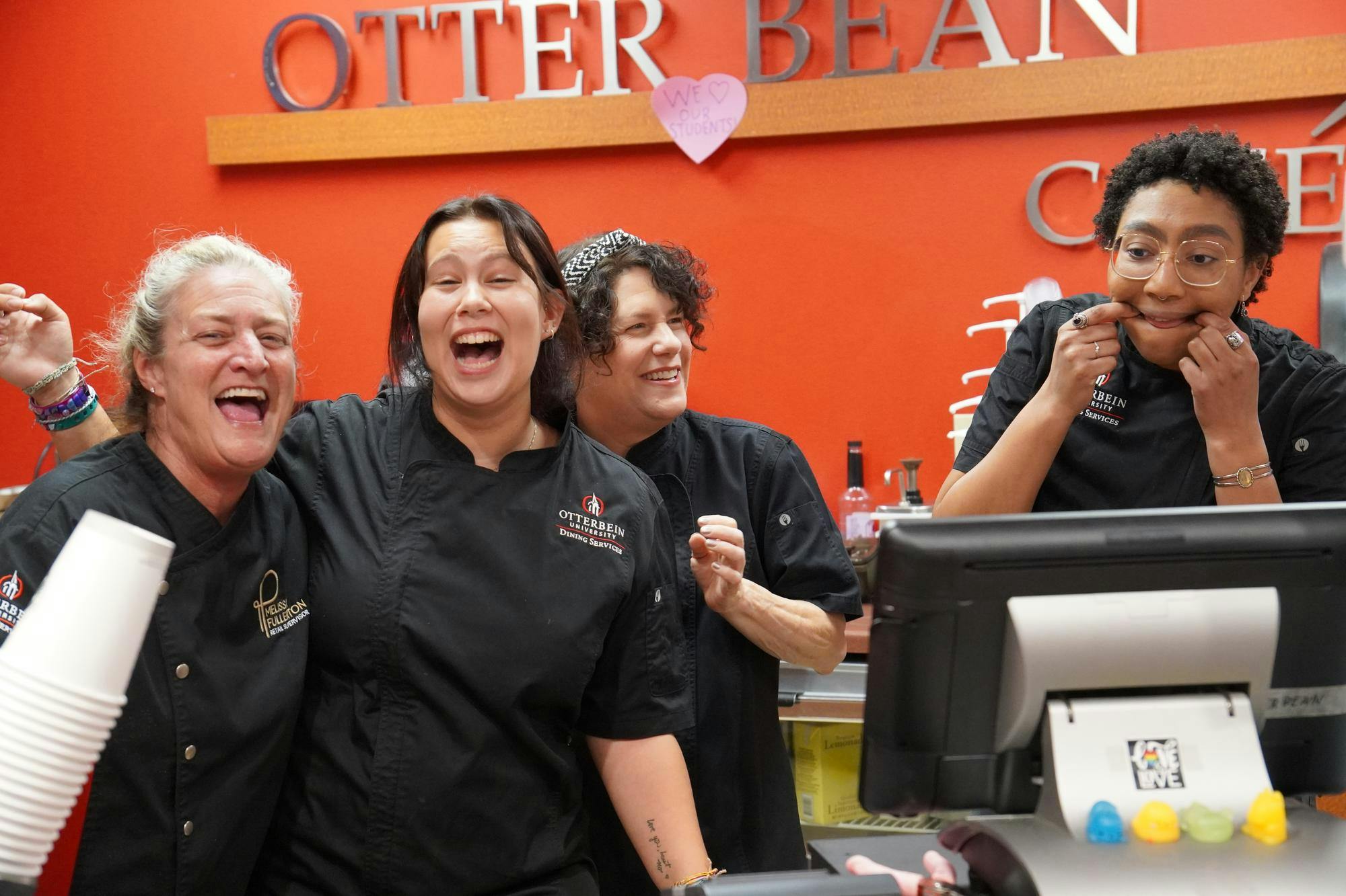 Four ladies with black uniforms laugh at one another making silly faces. 