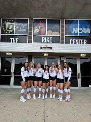 A group of women in volleyball jerseys pose in front of the Rike Center.