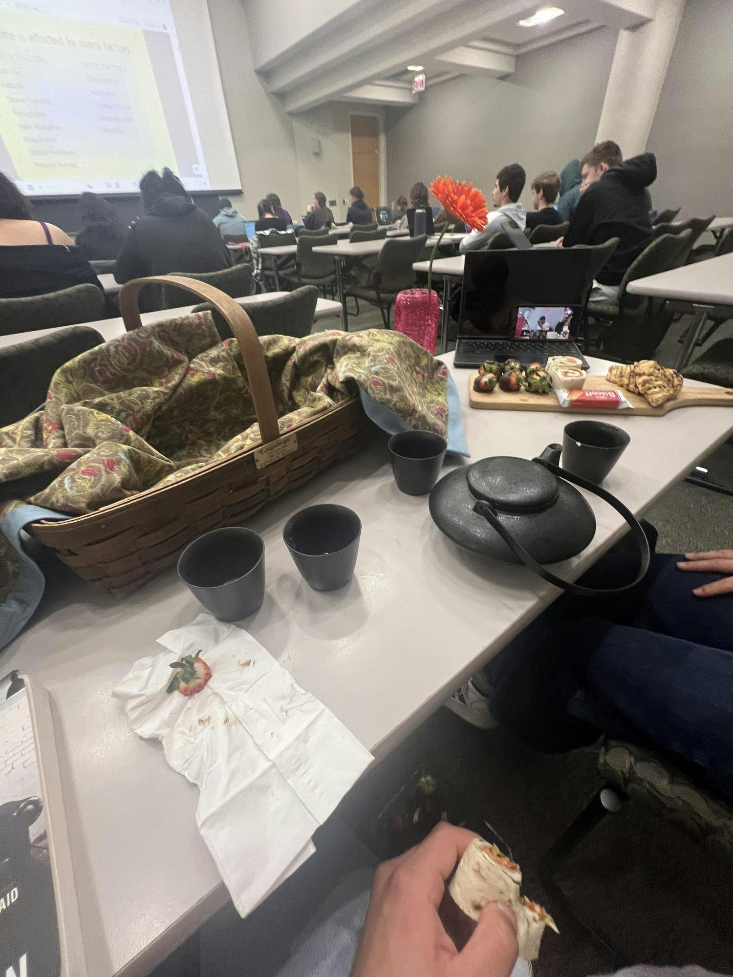 A classroom table with tea, chocolate covered strawberries and sandwich wraps.