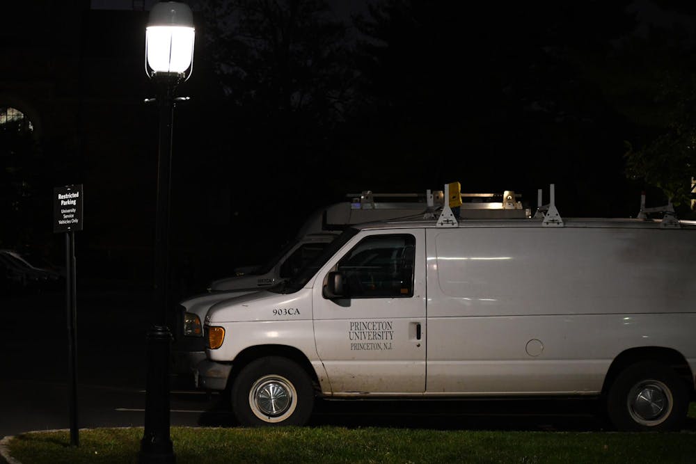 A white Ford E-150 van sits parked by a facilities building. It is dark outside and there is a single lamp lit in the foreground.