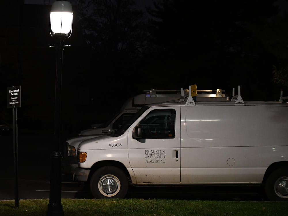 A white Ford E-150 van sits parked by a facilities building. It is dark outside and there is a single lamp lit in the foreground.