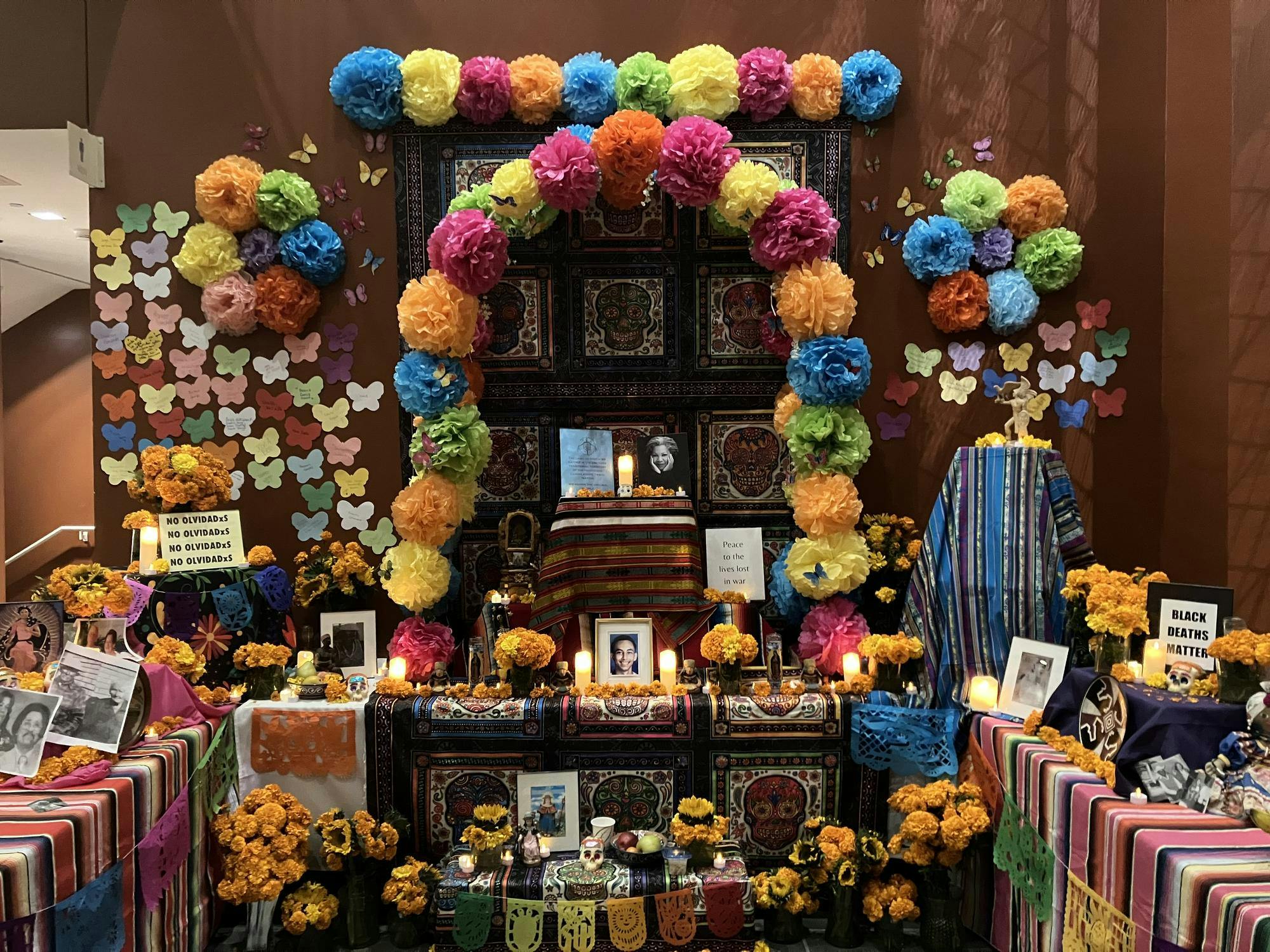 An altar honoring the deceased, decorated with colorful cloth, orange marigolds, and bright tissue paper flowers.
