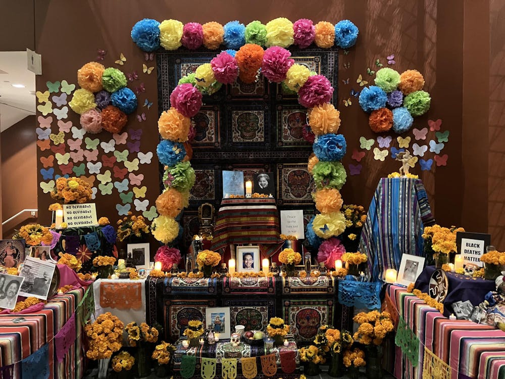 An altar honoring the deceased, decorated with colorful cloth, orange marigolds, and bright tissue paper flowers.