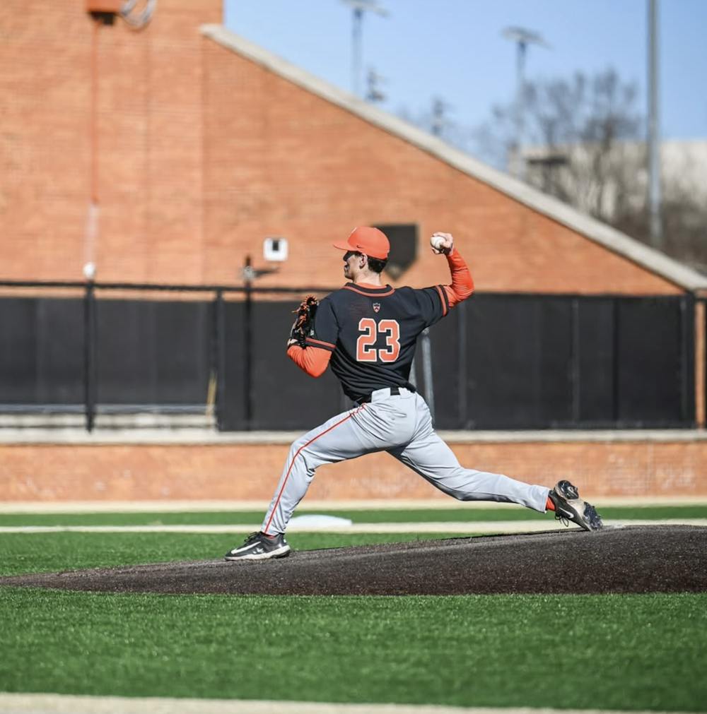 Man in black and orange jersey throwing a baseball