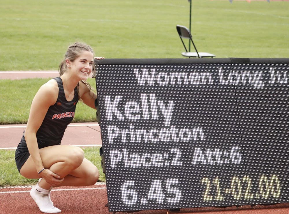 A women posing next to a scoreboard showing her score in a women's track and field event. 