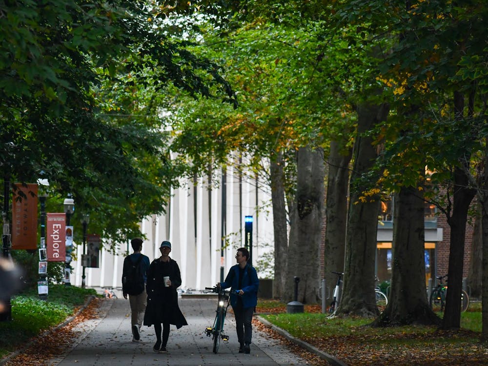Three students with backpacks walk down a tree-lined path on campus in front of the SPIA building. 