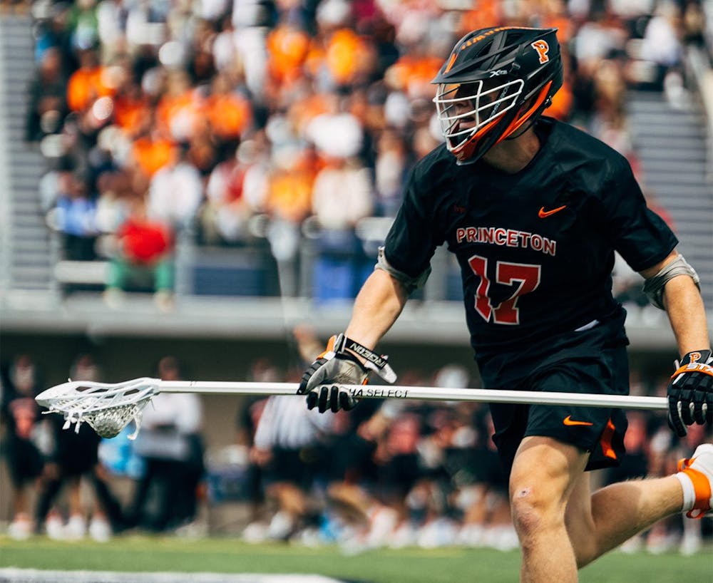 A man running with a lacrosse stick sports a Princeton jersey with the number 17 on it.
