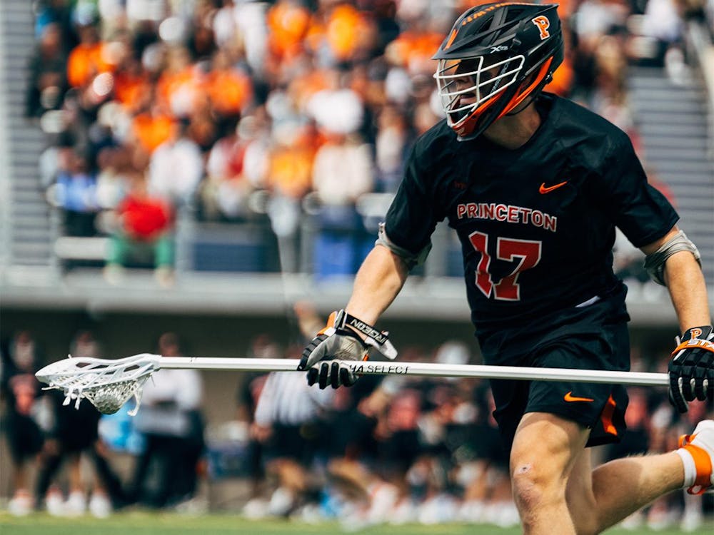 A man running with a lacrosse stick sports a Princeton jersey with the number 17 on it.
