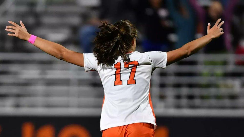 Female soccer player with her arms spread out facing a blurry crowd. A bright orange 17 is on her shirt