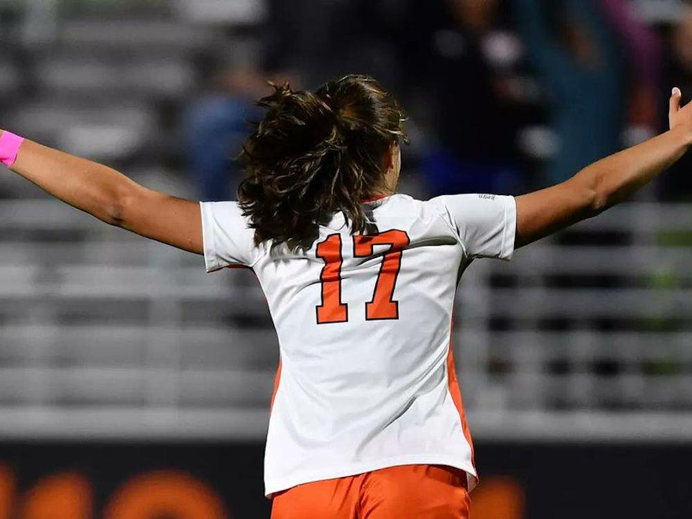 Female soccer player with her arms spread out facing a blurry crowd. A bright orange 17 is on her shirt