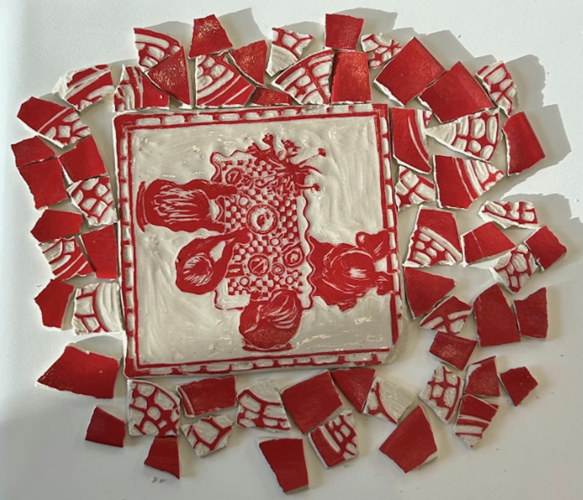 A red and white pottery is flat with a table and figures carved into it.