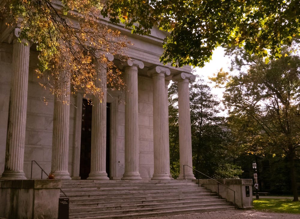 A building will tall stone pillars. Orange trees drop leaves all around. 