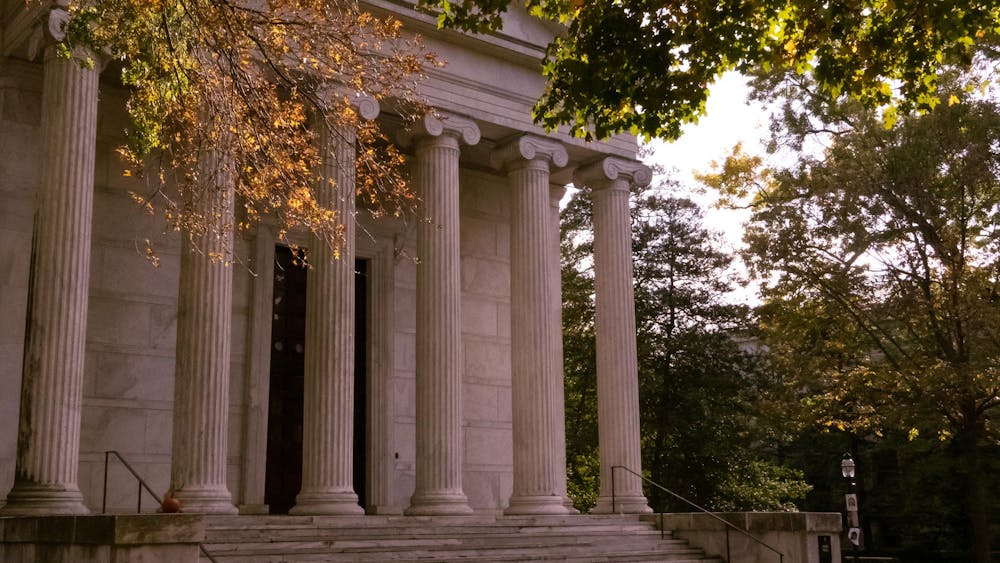 A building will tall stone pillars. Orange trees drop leaves all around.