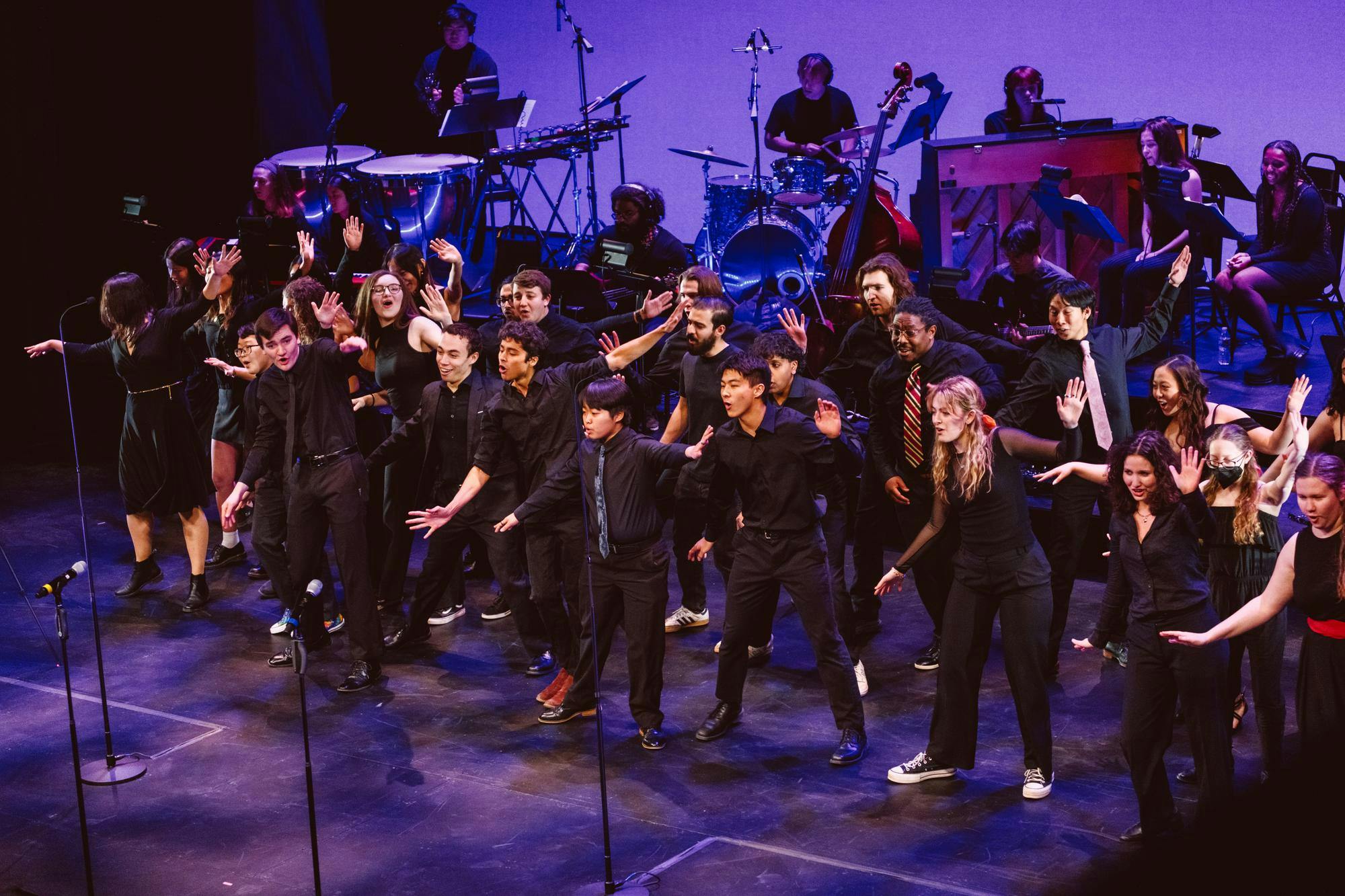 A group of people dressed in all black with colorful ties in front of a band on a purple-lit stage.