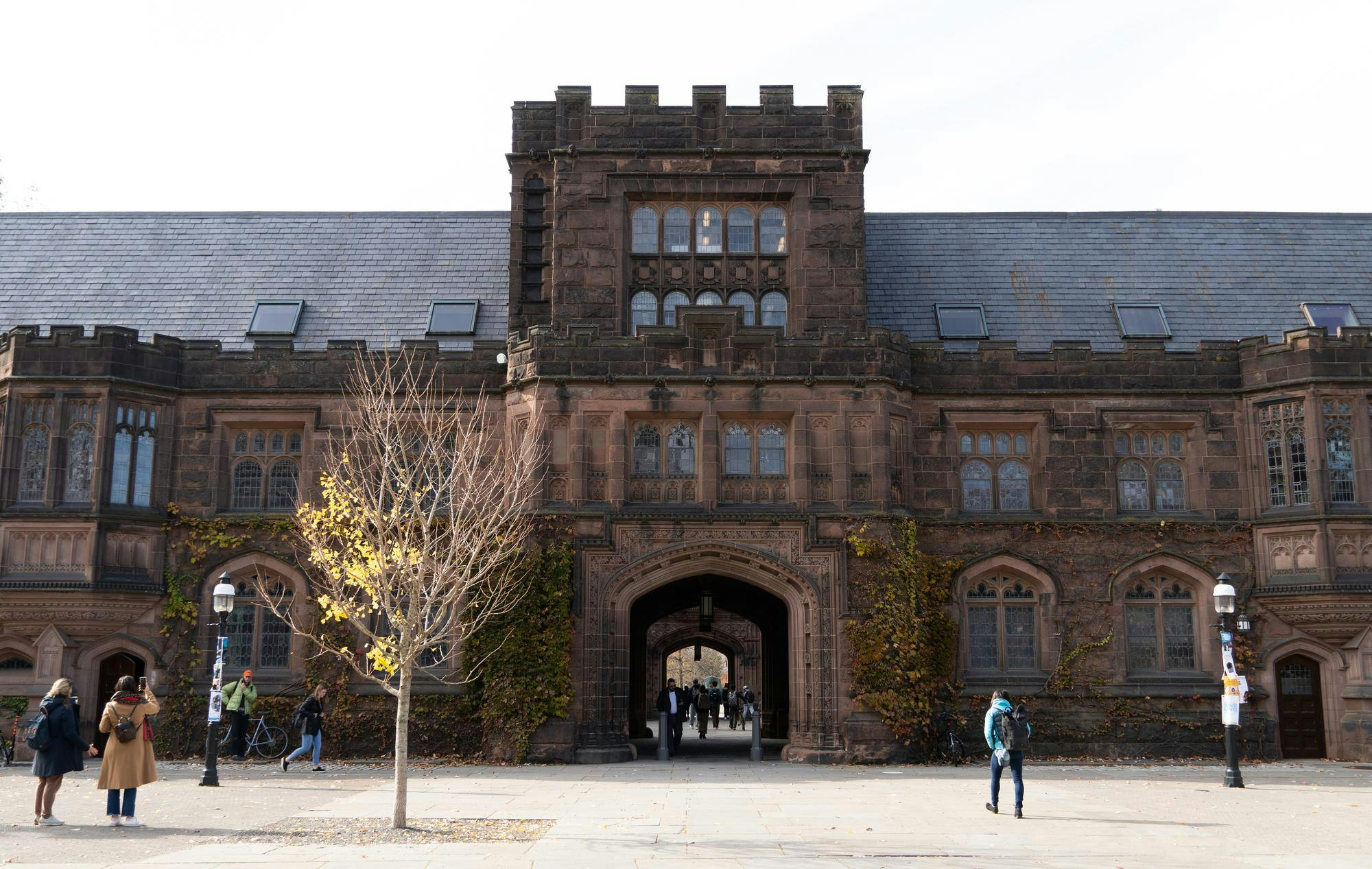 A brown gothic-style building stands in the background, with a tree in the foreground.