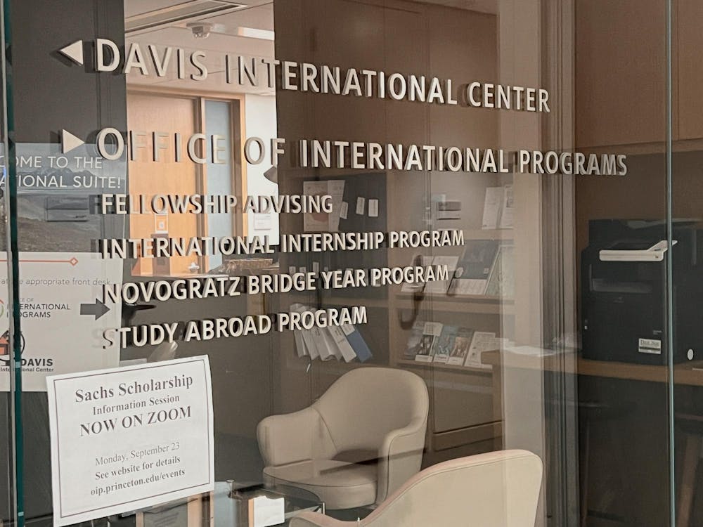 A glass wall with a chair and bookshelf reflected in it. Text on the wall reads “Office of International Programs.”