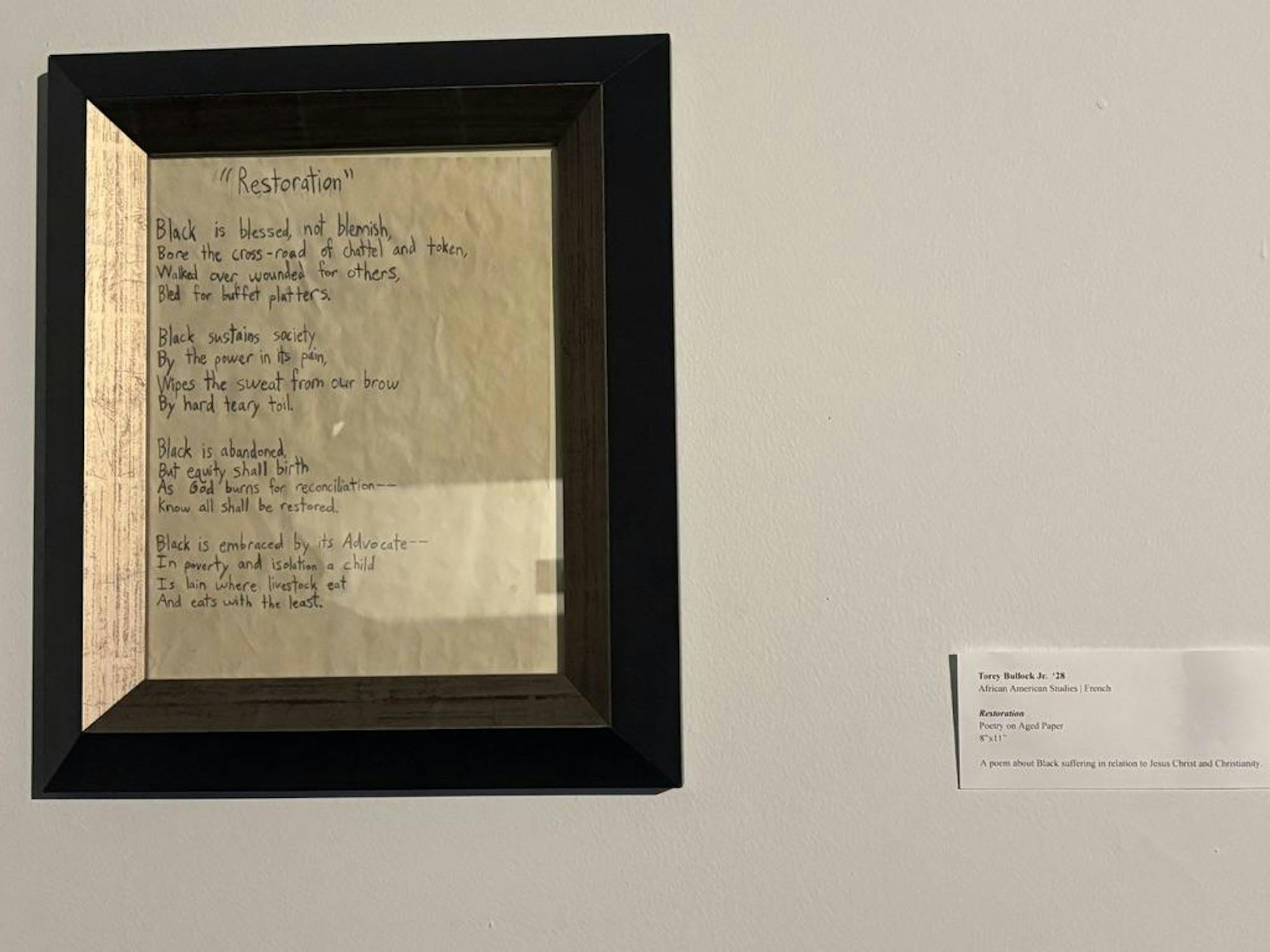 A framed paper with words on it is hung on a white wall.