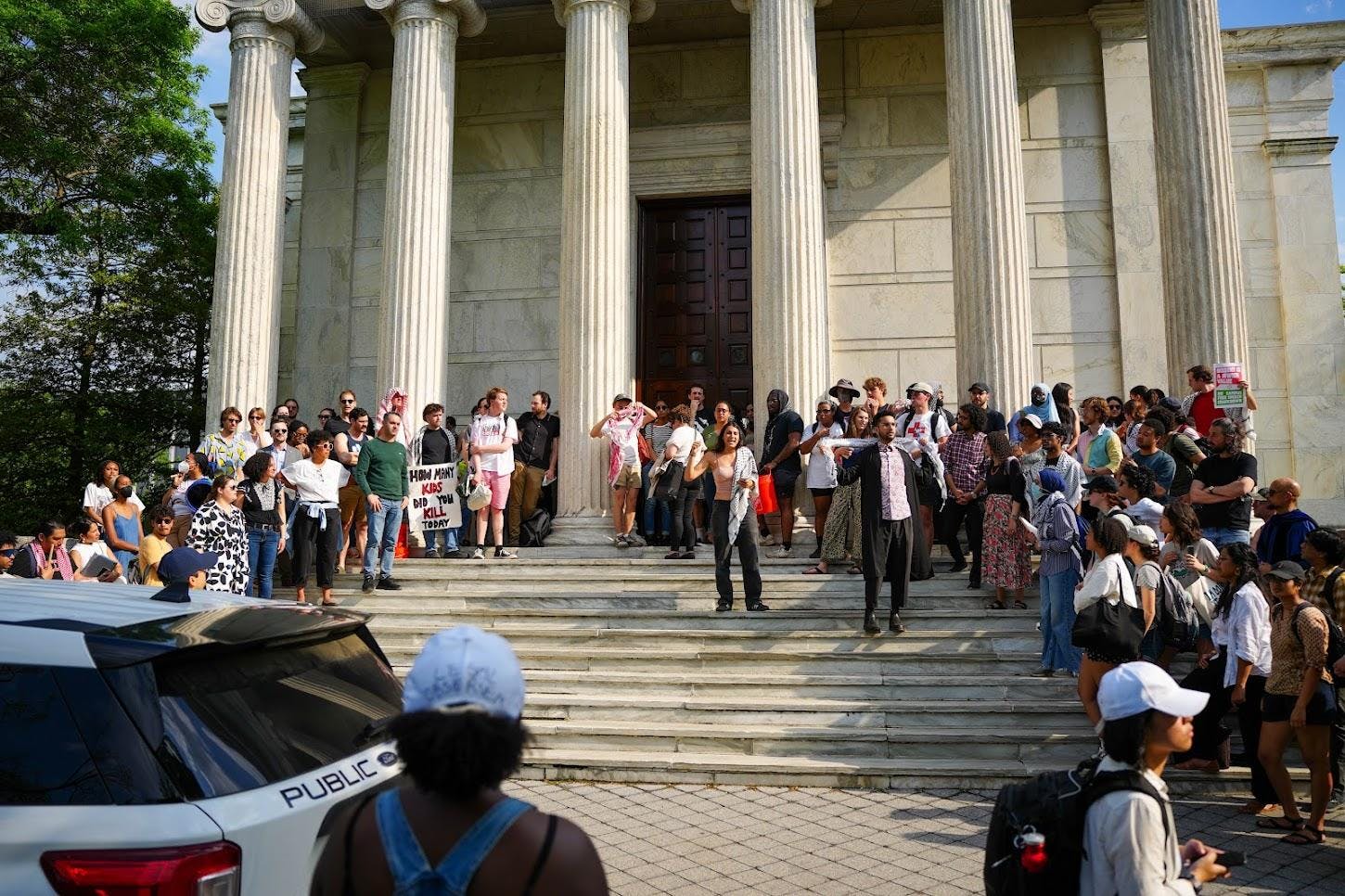People gathered on steps in front of white building with columns holding signs
